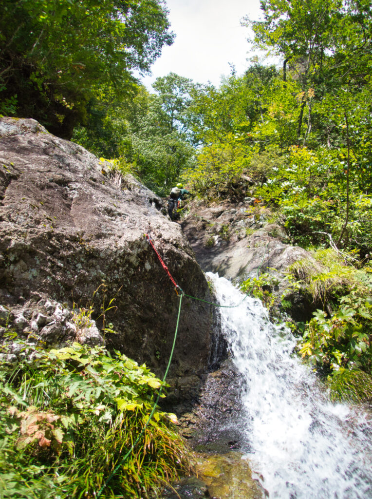 Climber traversing across Ryomon Falls waterfall face in Suginomorisawa stream climbing