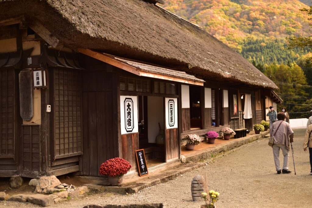 Ouchi-juku traditional thatched roof houses along historic Edo-period highway, autumn mountains background, Fukushima