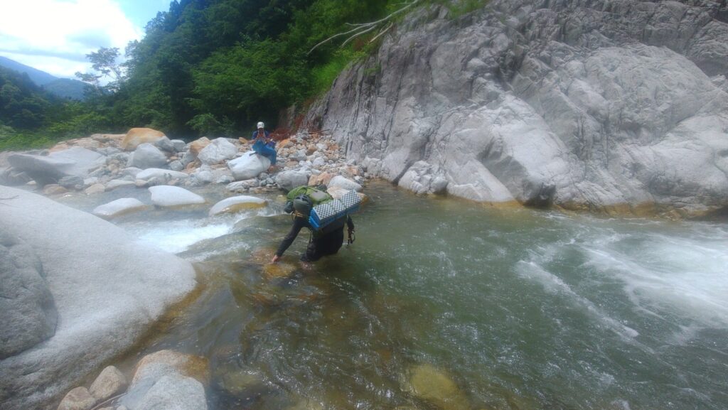 Climber wading through knee-deep Shirahagi River crossing on the Tsurugi Ikenotan approach