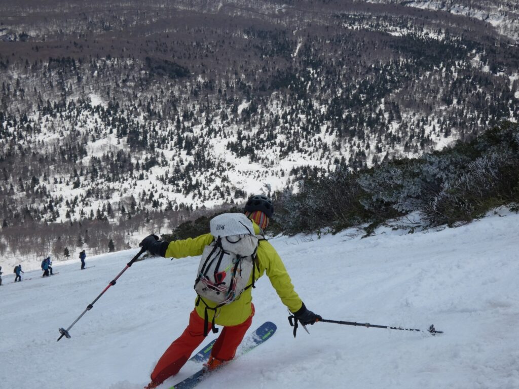 Skier carving turns on steep slope of Mt. Takadaodake with white spray flying from ski edges