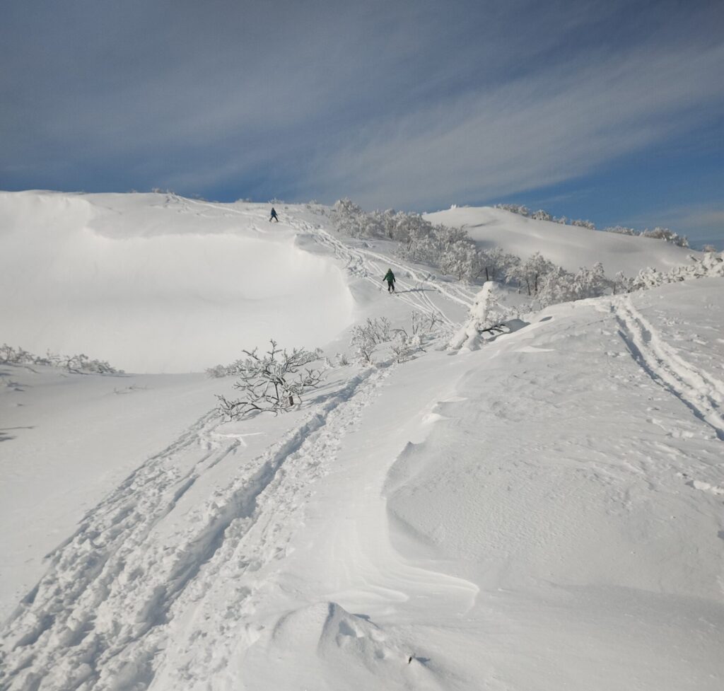 Ski mountaineer descending snowy slope with mountain panorama in Funagata range
