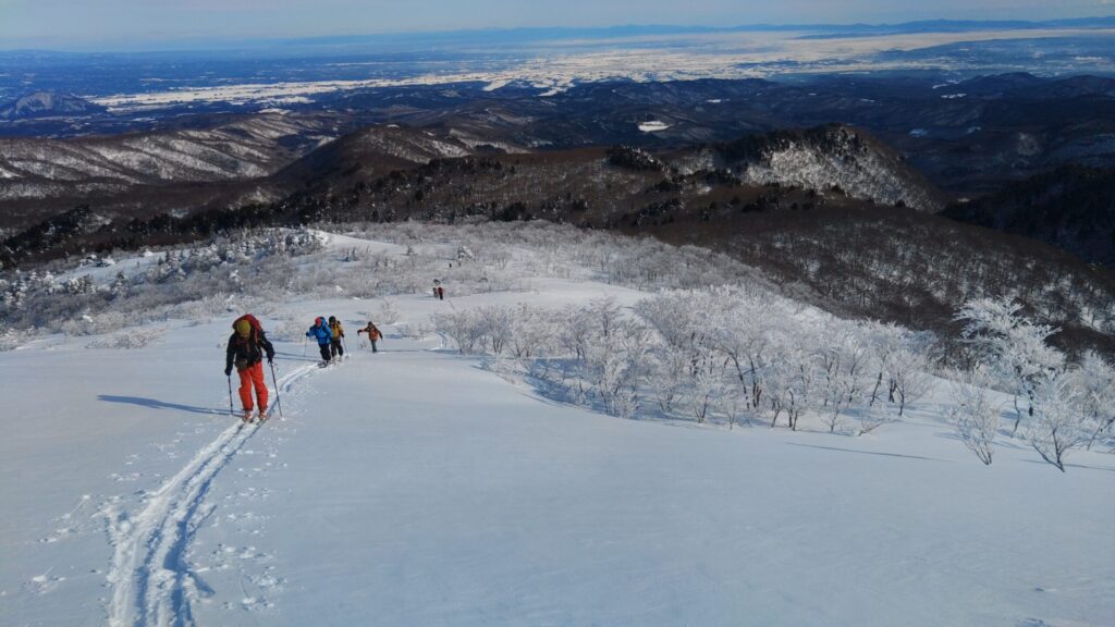 Skiers climbing final slope to Jagadake summit through open terrain in winter