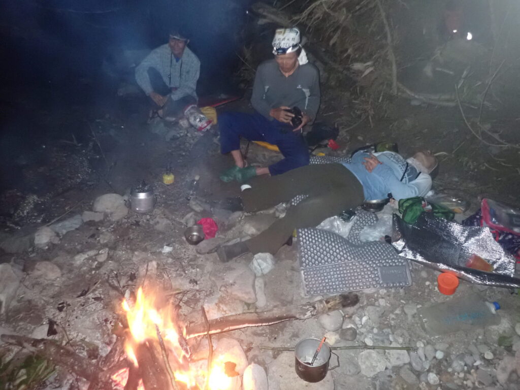 Climbers gathered around campfire at night during bivouac on Kitanomata-zawa stream climbing trip, Hachimantai Japan