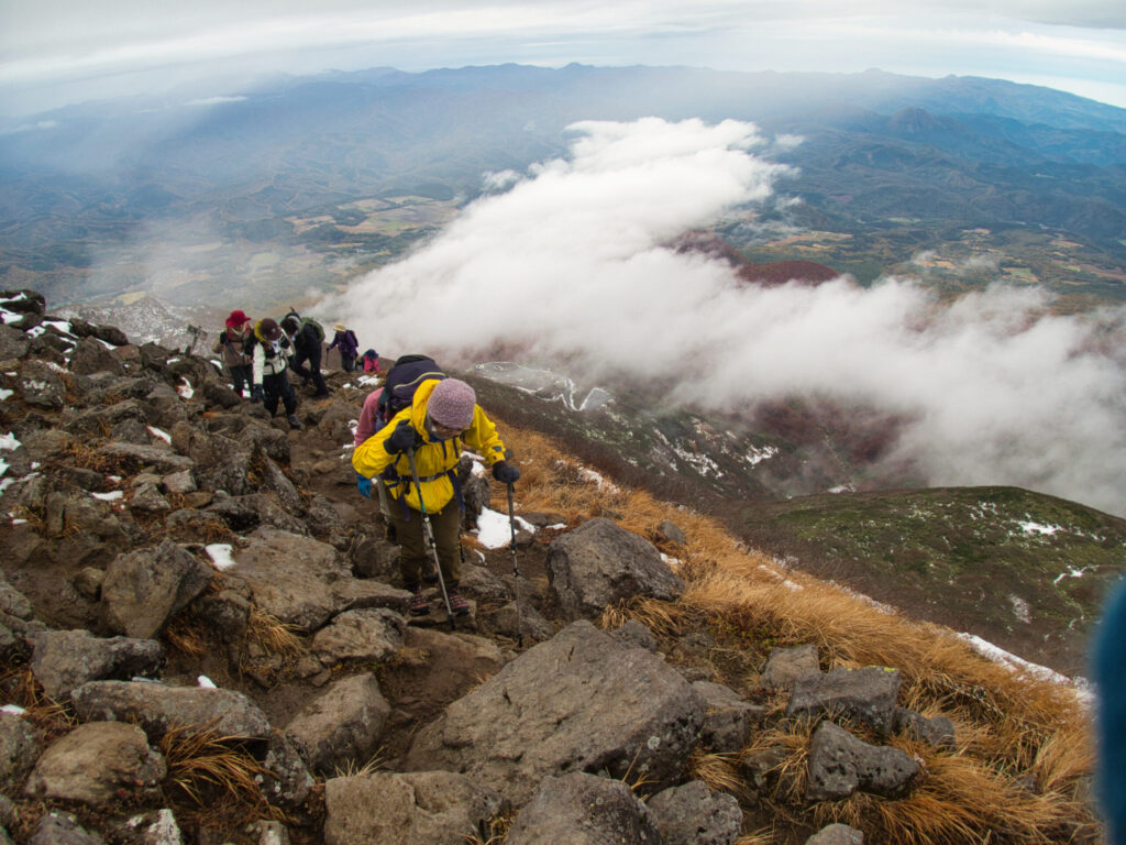 18 climbers continuing the final rocky push toward the summit of Mt. Iwaki-san through snow