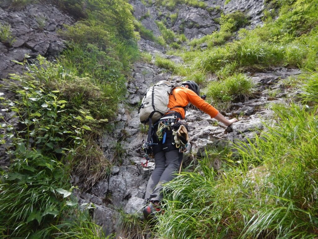 "Climber on slab section leading to couloir, narrow terrace belay station"